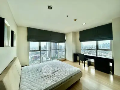 Spacious bedroom with panoramic city views and modern furnishings in a high-rise apartment.