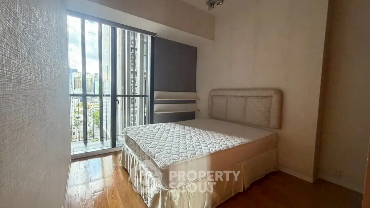 Cozy bedroom with large window and city view, featuring a comfortable bed and wooden flooring.