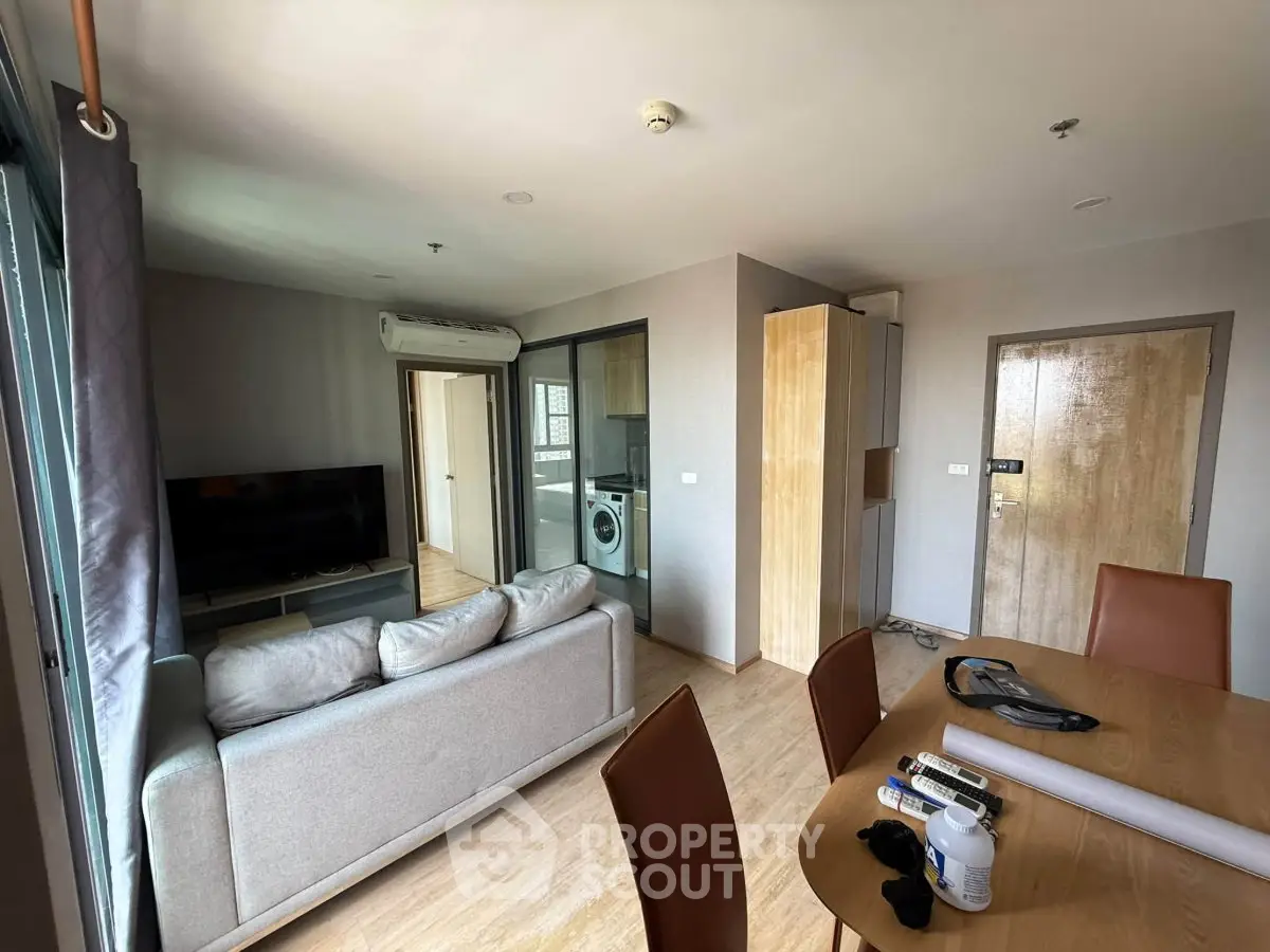 Modern living room with open layout, featuring a cozy sofa, dining area, and in-unit washing machine.