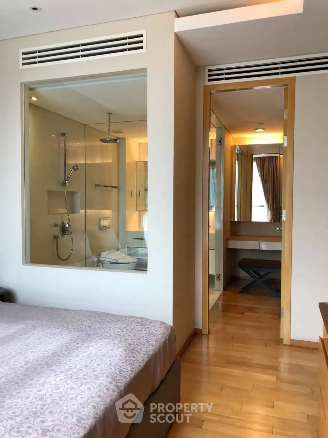 Modern bedroom with ensuite bathroom featuring glass partition and wooden flooring.