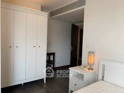 Modern bedroom with white furniture and sleek design, featuring a wardrobe and bedside table with lamp.