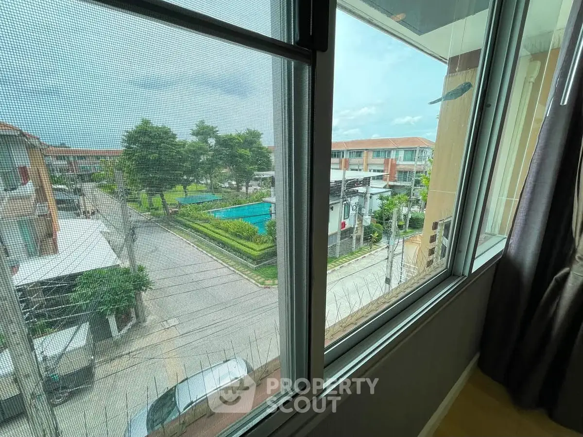 Scenic view from window overlooking residential area with pool and greenery.