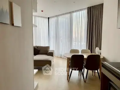 Modern living room with large windows and elegant dining area, featuring stylish furniture and natural light.