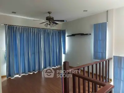 Spacious living room with wooden flooring and blue curtains, featuring a ceiling fan and modern wall shelves.