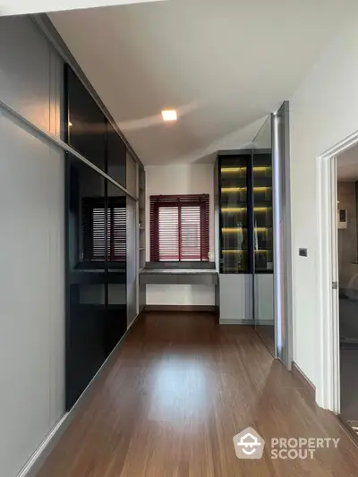 Sleek modern living space with glossy built-in cabinets and warm wooden flooring, complemented by natural light filtering through stylish red blinds.