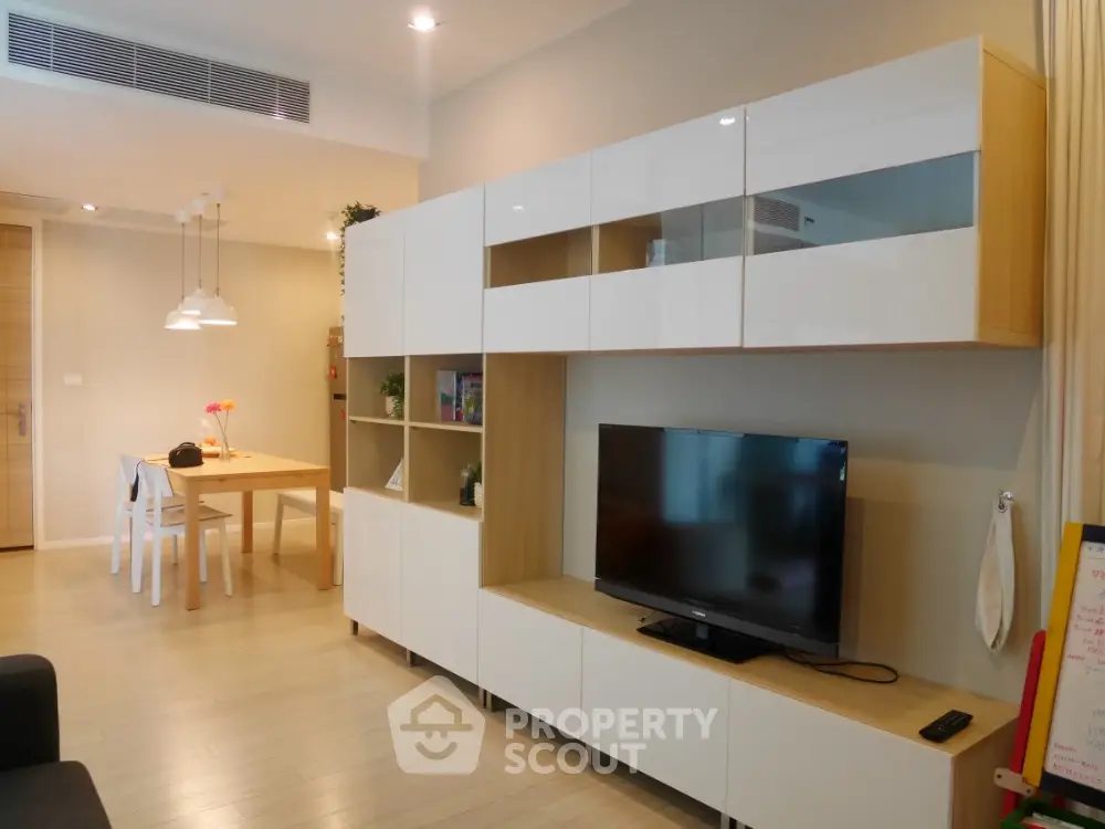Modern living room with sleek TV unit and dining area in open layout apartment.