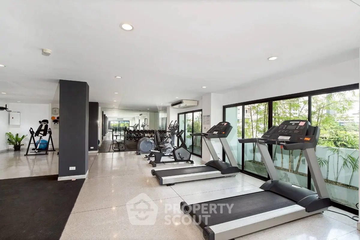 Spacious modern gym with state-of-the-art equipment and large windows offering lush greenery views.