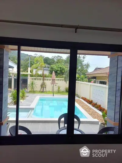 Luxurious poolside view from modern home window, showcasing tropical landscaping and serene outdoor ambiance.