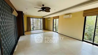 Spacious living room with large windows and ceiling fan, offering abundant natural light.