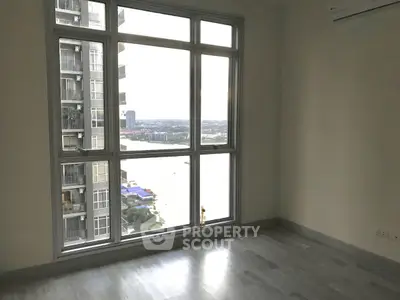 Spacious room with large window offering stunning cityscape view in modern high-rise building.
