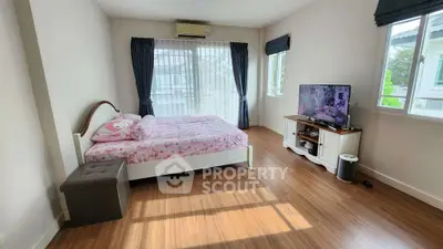 Spacious bedroom with large windows and wooden flooring, featuring a cozy bed and modern TV setup.