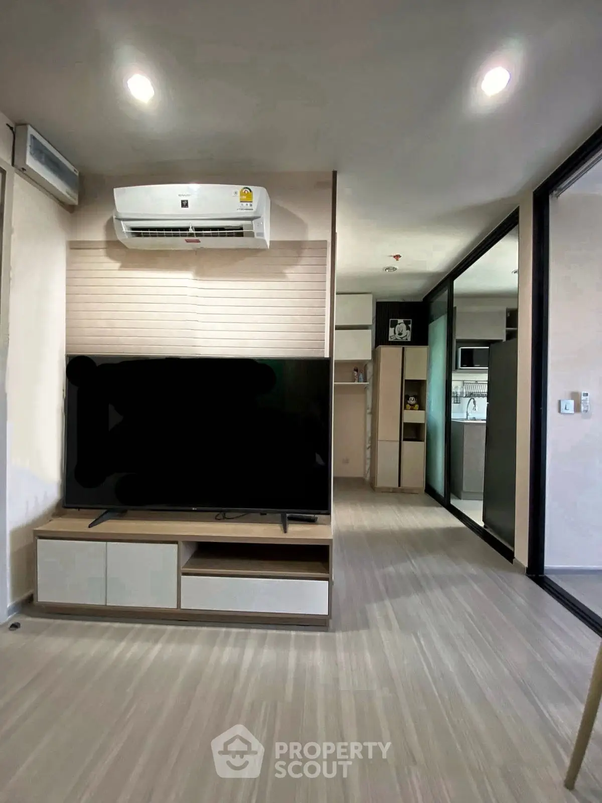 Modern living room with sleek design and air conditioning, featuring a large TV and open kitchen view.