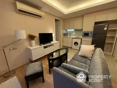 Modern living room with open kitchen, featuring washing machine and sleek appliances.