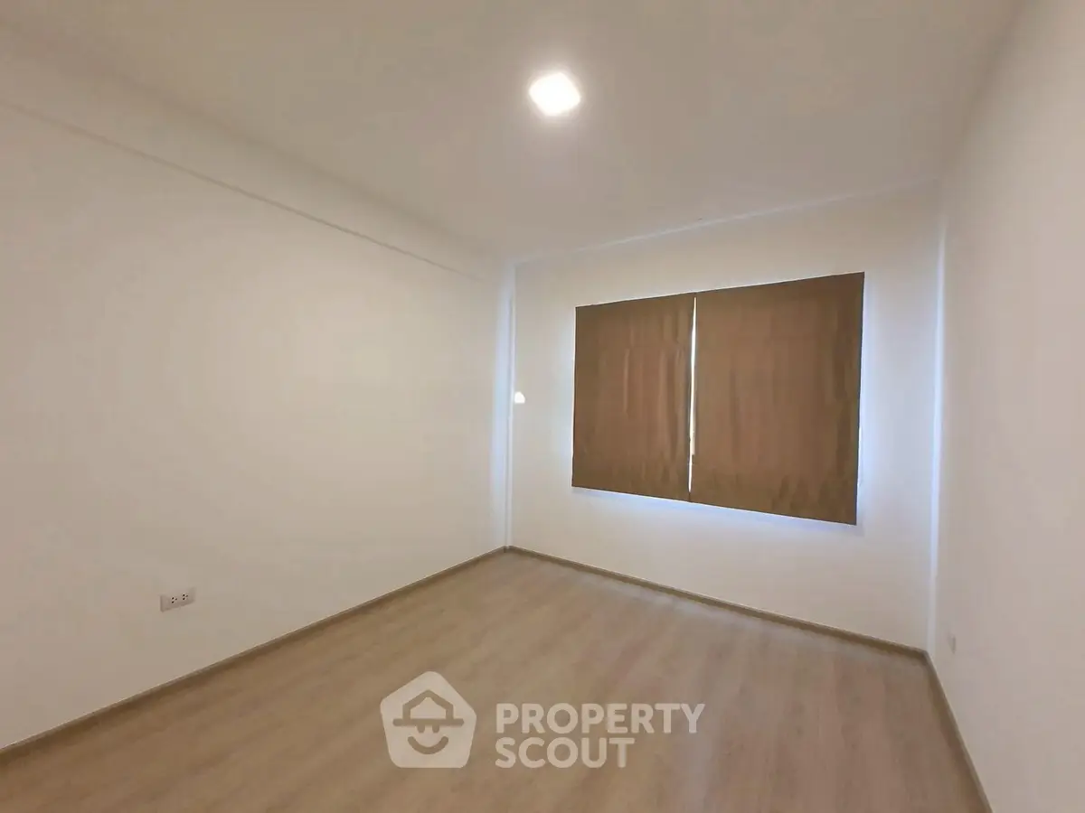 Spacious empty room with wooden flooring and large window, perfect for customization.
