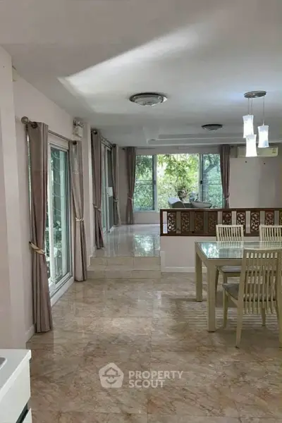 Spacious living room with dining area and large windows overlooking greenery.