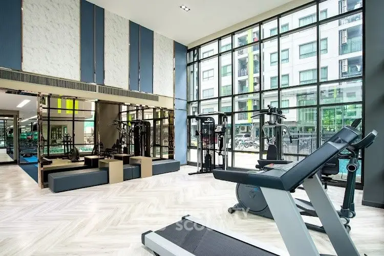 Modern gym with large windows and state-of-the-art equipment in luxury apartment building.