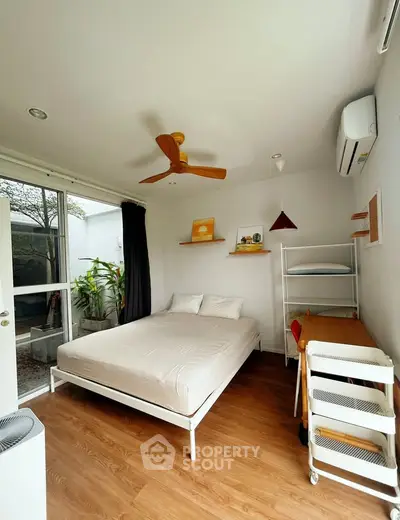 Cozy bedroom with modern decor, wooden flooring, and natural light from large window.