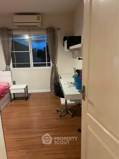 Cozy bedroom with study area and window view, featuring wooden flooring and modern furnishings.