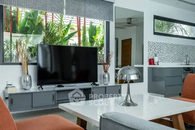 Modern living room with sleek furniture and large TV, featuring a view of lush greenery through the window.