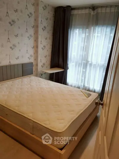Cozy bedroom with stylish wallpaper and natural light from large window.