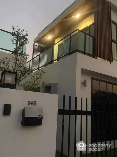 Modern two-story house with sleek design and illuminated balcony at dusk.