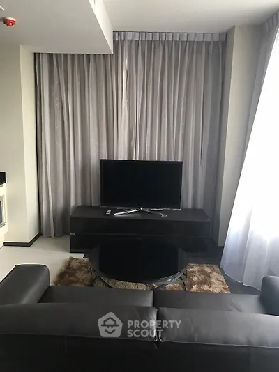 Modern living room with sleek black furniture and large TV, elegant curtains enhance the ambiance.