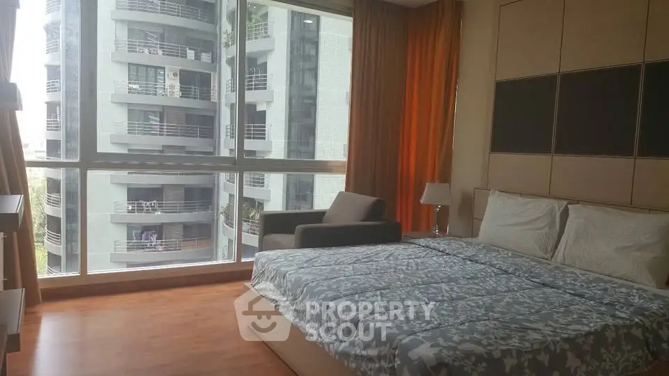 Spacious bedroom with large windows offering a stunning city view, modern furnishings, and elegant decor.