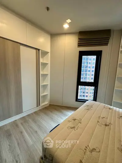 Modern bedroom with built-in wardrobe and city view window, featuring elegant wood flooring.