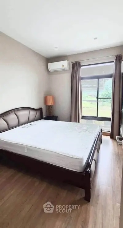 Spacious bedroom with large window and wooden flooring in modern apartment.