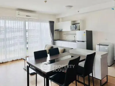 Modern open-plan living room with dining area and kitchen, featuring large windows and sleek furniture.
