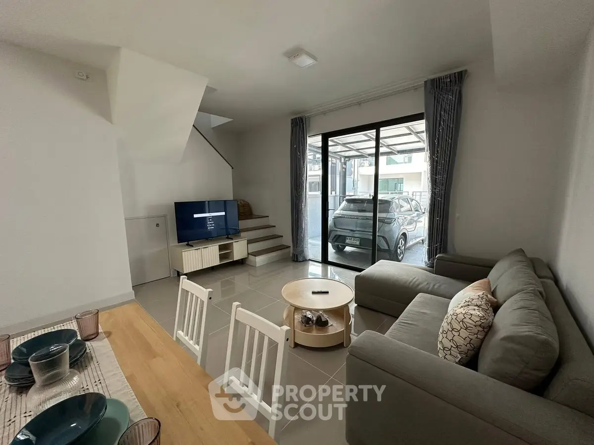 Modern living room with sleek furniture and large windows leading to a carport.