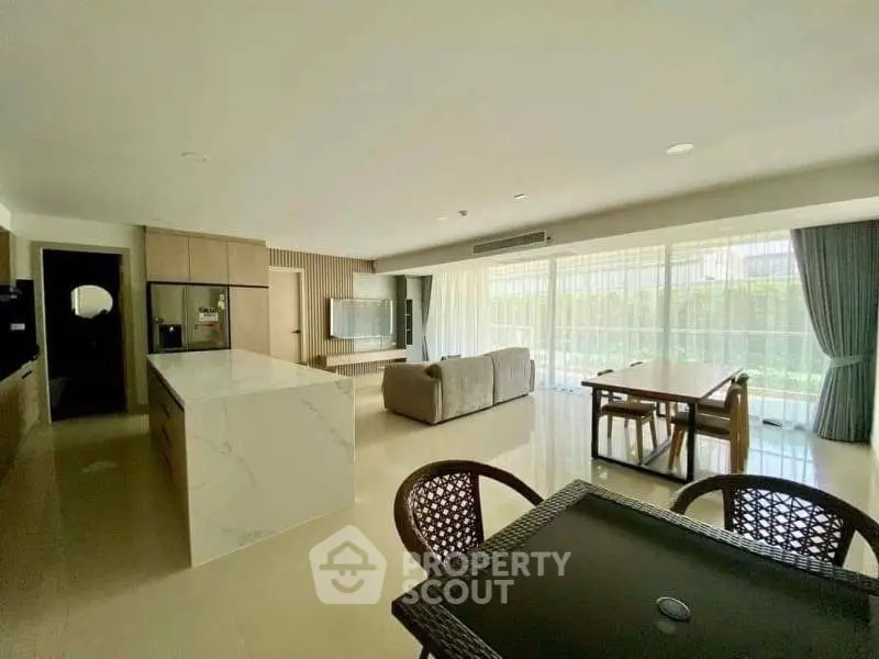 Spacious open-plan living room with modern kitchen and large windows offering natural light.