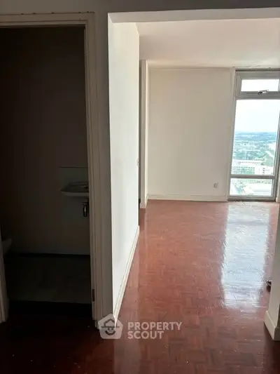 Spacious apartment with wooden flooring and large window offering stunning city views.