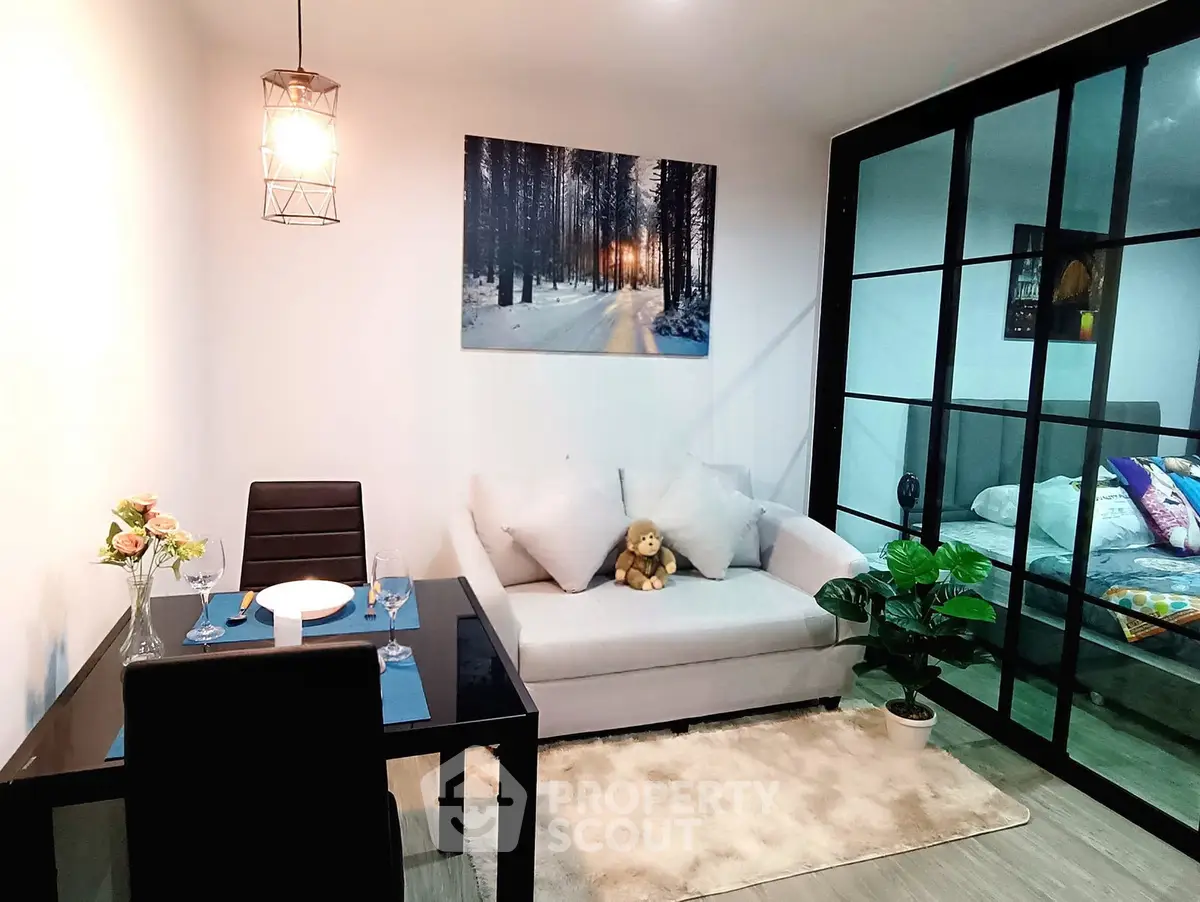 Modern living room with cozy sofa, dining table, and glass partition leading to bedroom.