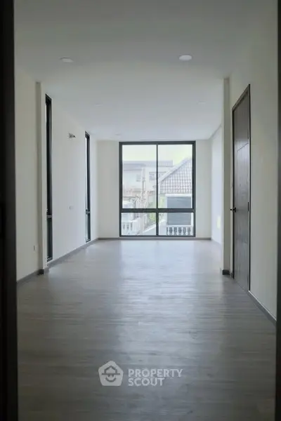 Spacious empty room with large window and wooden flooring, ideal for customization.