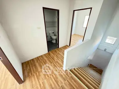 Modern home interior with wooden flooring and staircase, featuring a bathroom and natural light.