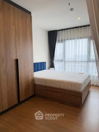 Modern bedroom with wooden flooring and large window offering city view