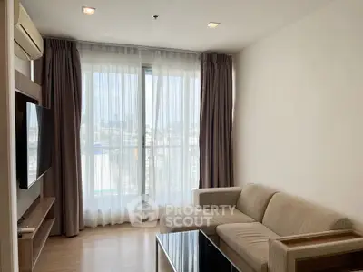 Modern living room with large windows and city view, featuring a comfortable sofa and sleek TV setup.