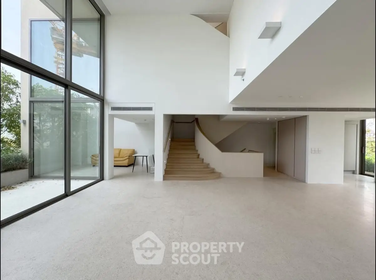 Spacious modern living room with large windows and staircase, perfect for natural light lovers.