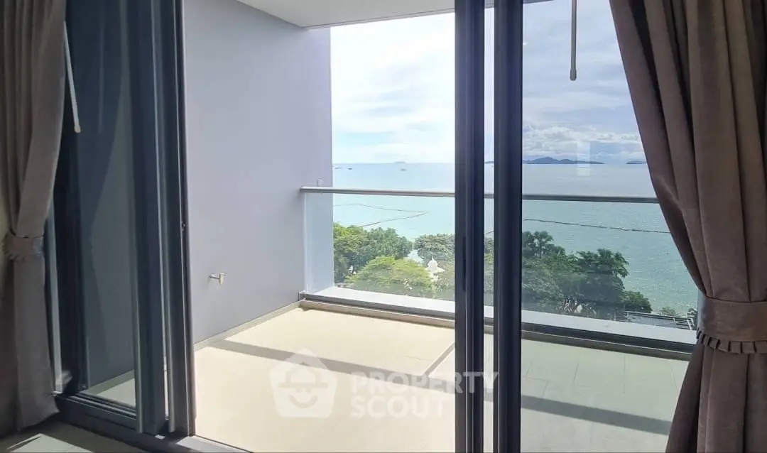 Stunning ocean view from modern apartment balcony with glass doors and elegant curtains.