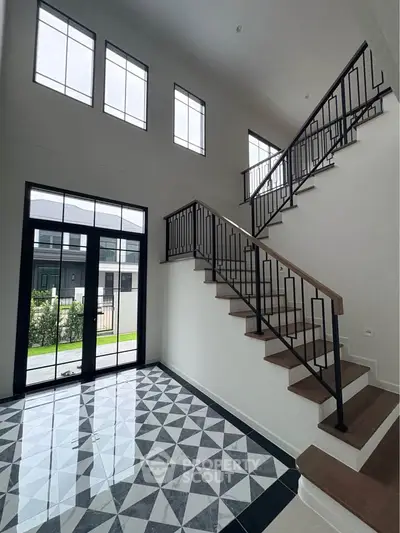 Elegant modern staircase with geometric floor tiles and large windows in a spacious home entryway.