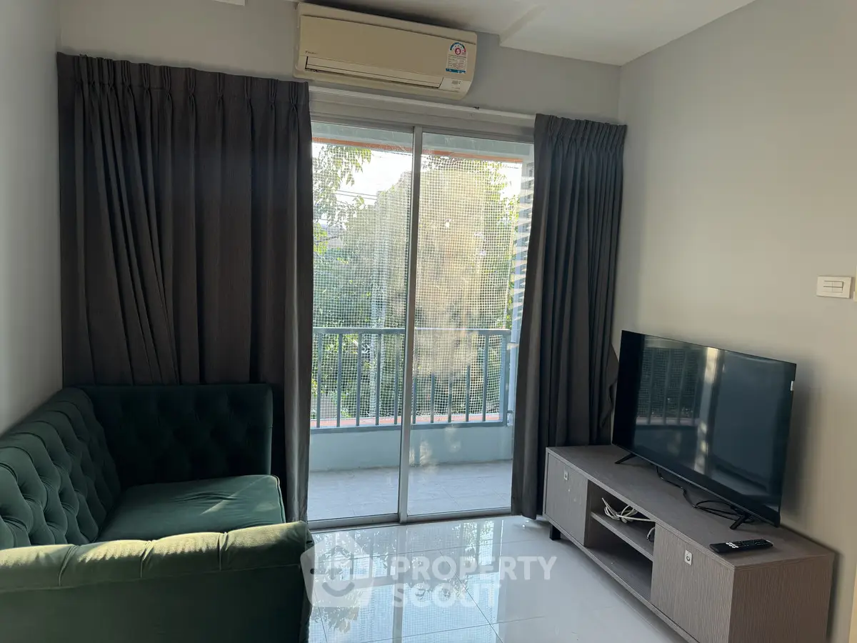 Modern living room with balcony view, featuring a sleek TV setup and stylish green sofa.