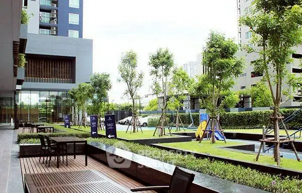 Modern apartment complex with lush garden and outdoor seating area.