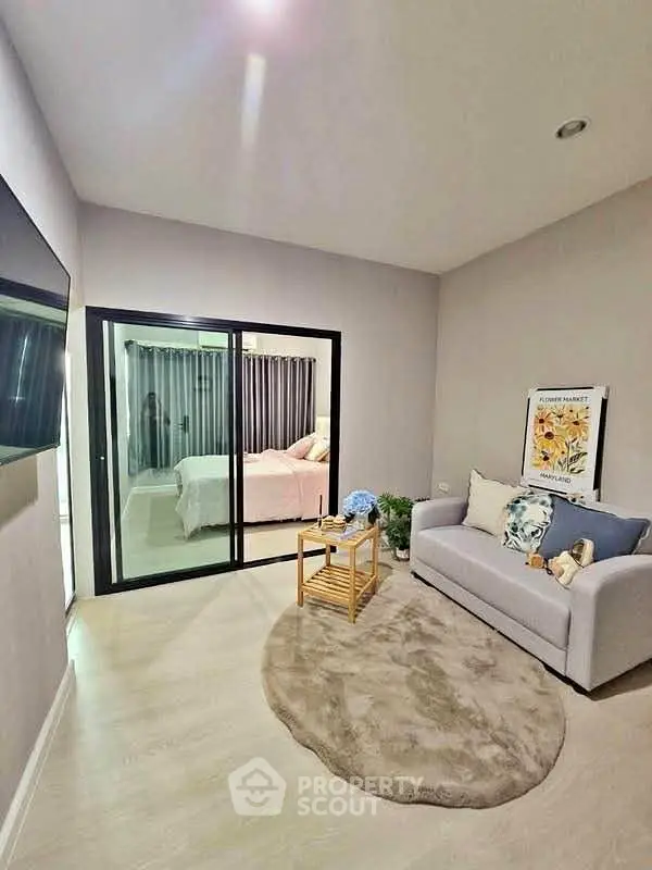 Modern living room with cozy sofa and view into stylish bedroom through glass doors.