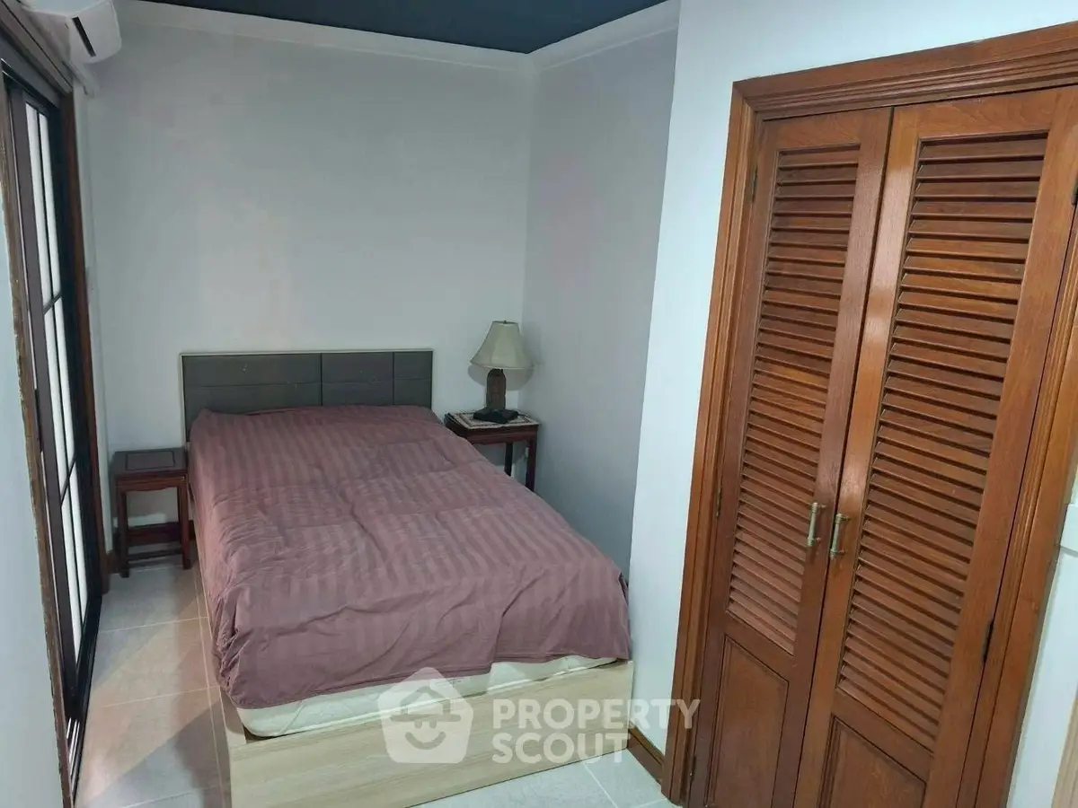 Cozy bedroom with wooden closet and bedside lamp, perfect for relaxation.