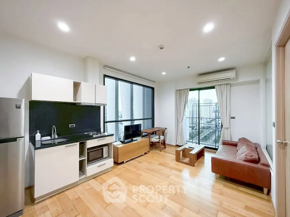 Modern open-plan living room with kitchen and city view balcony in high-rise apartment.
