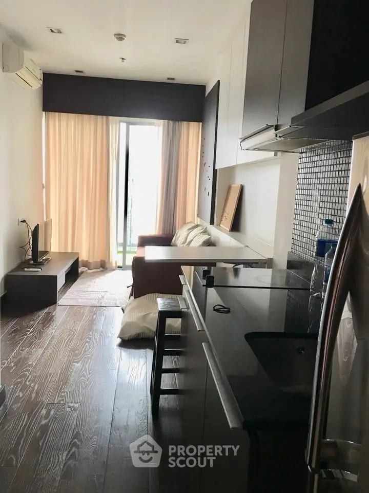 Modern living room with open kitchen and balcony access, featuring sleek design and natural light.