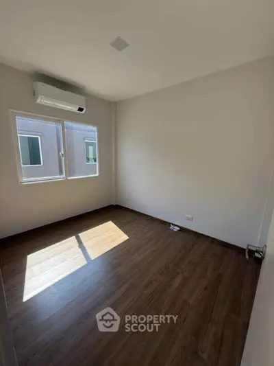 Bright empty room with wooden flooring and air conditioning, perfect for customization.