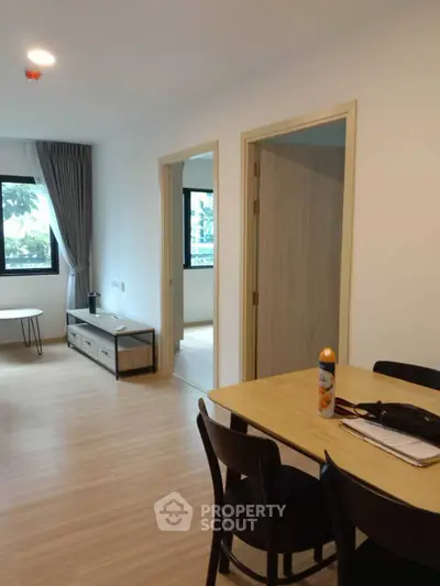 Modern apartment interior with dining area and living room, featuring wooden flooring and natural light.