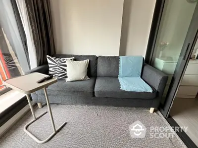 Chic modern living room with a comfortable grey sofa, stylish cushions, and a sleek side table, complemented by natural light.